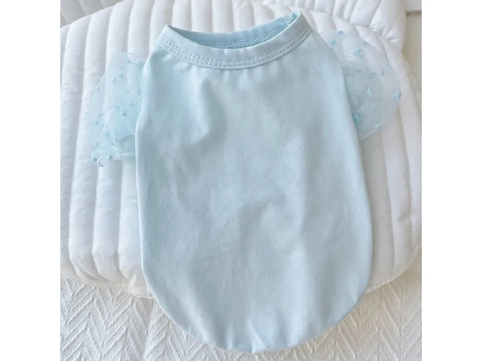 A light blue pet dress with mesh puff sleeves laid flat on a white cushion.