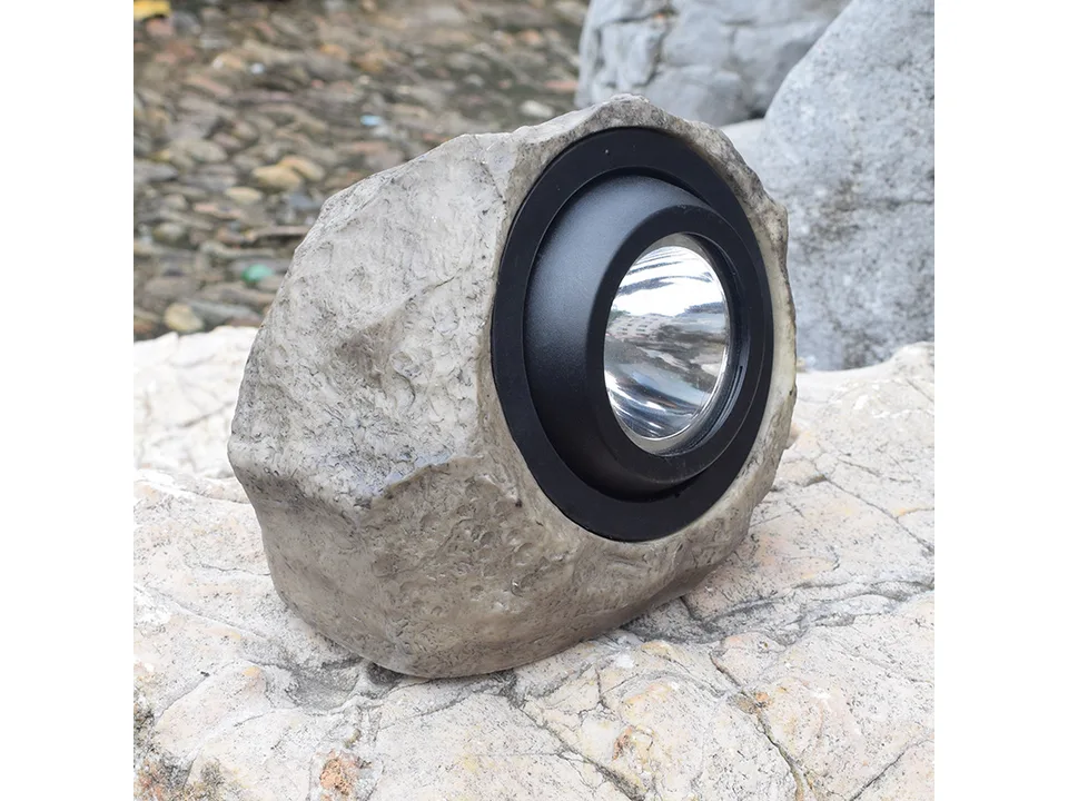 A rock-shaped solar garden spotlight sitting on a stone surface.