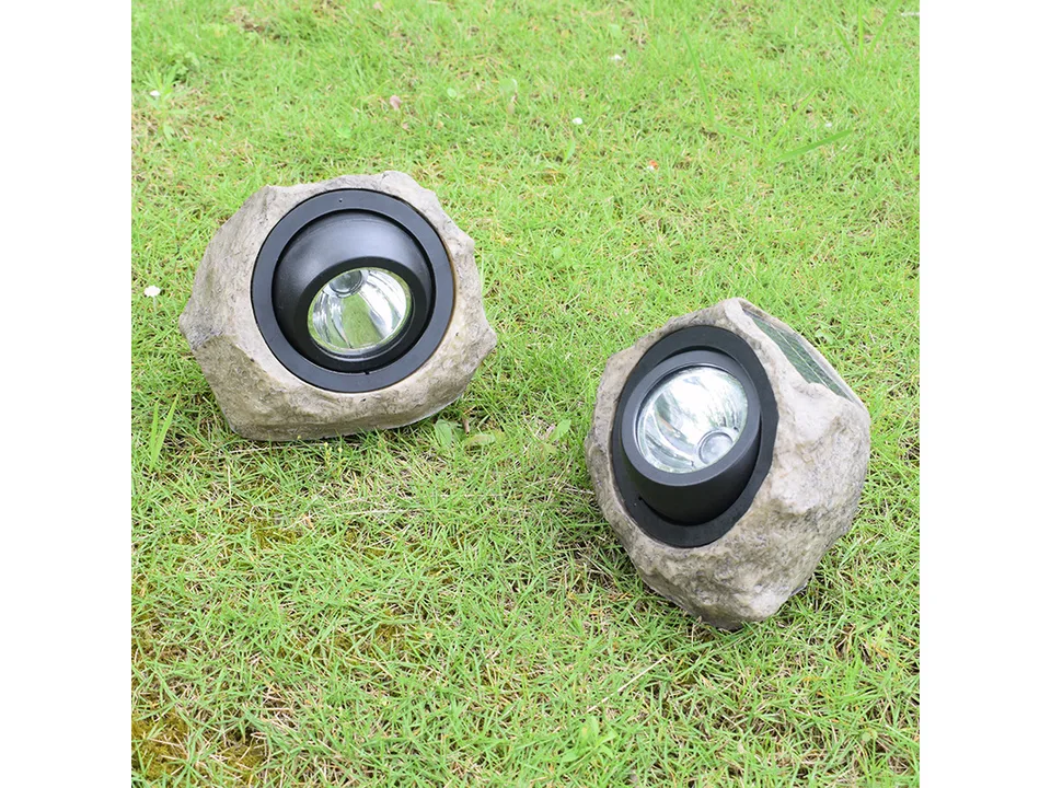 Two rock-shaped solar garden spotlights placed on a green lawn.