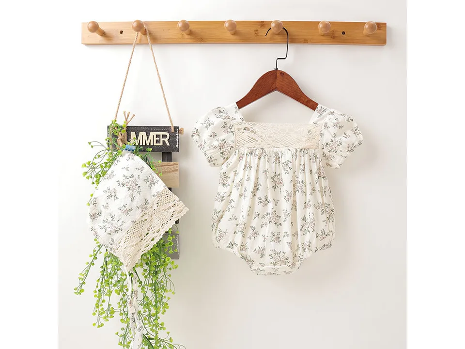 Baby floral romper with lace detail and matching bonnet hanging on a rack.