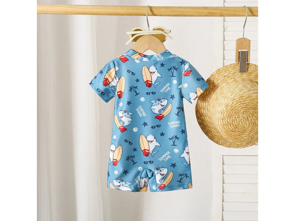 Blue boys' swimsuit with shark and surfboard print hanging on a wooden hanger.