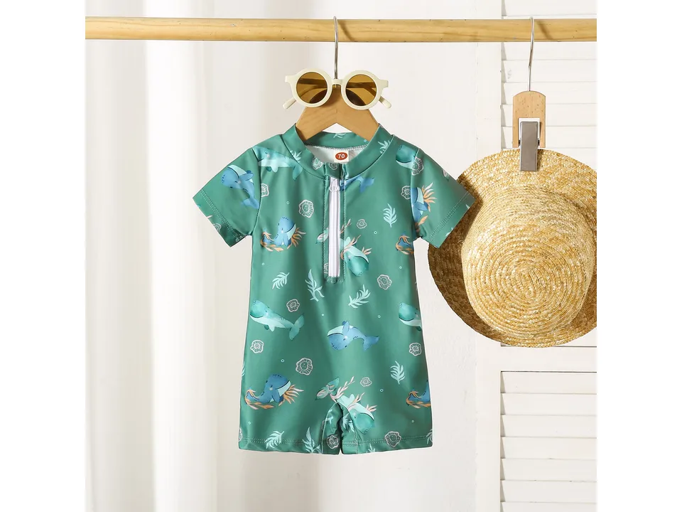 Green boys' swimsuit with whale print hanging on a wooden hanger.