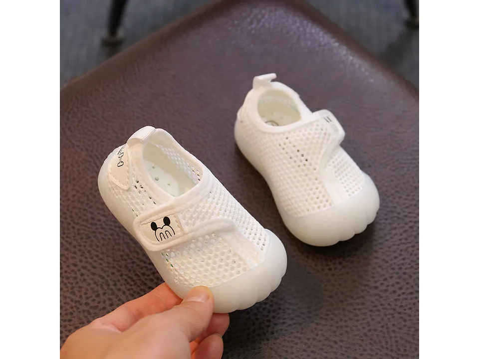 Hand holding a white breathable mesh baby sneaker.