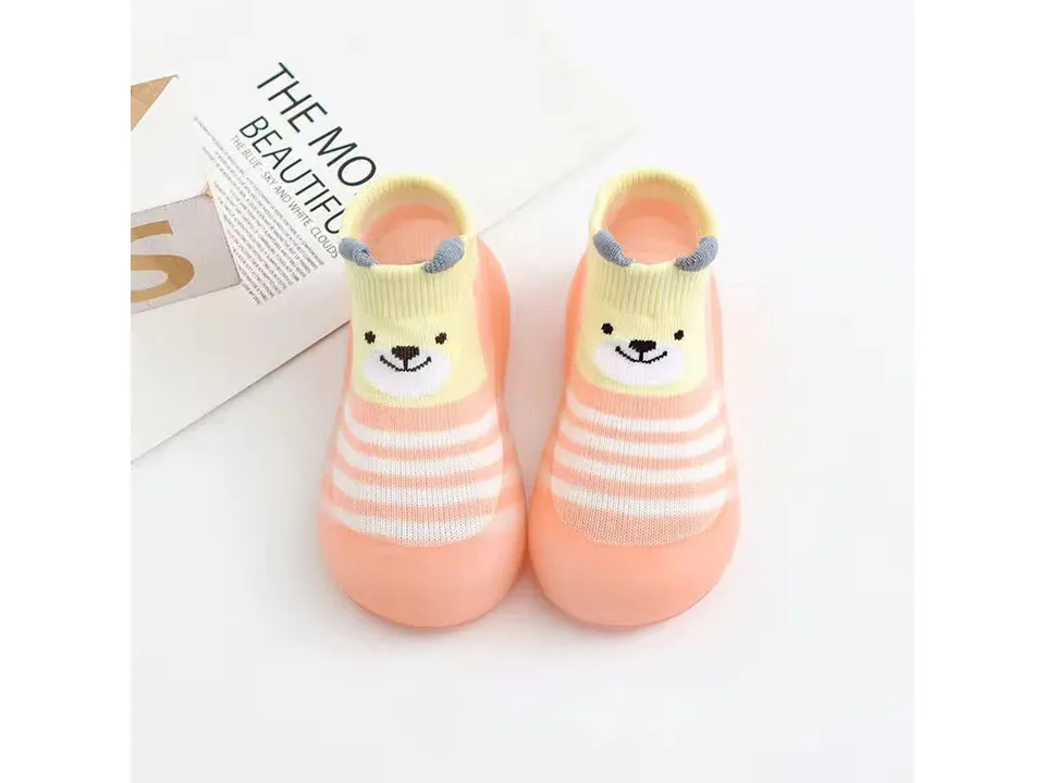 A pair of peach-colored toddler sock shoes with a bear face design.