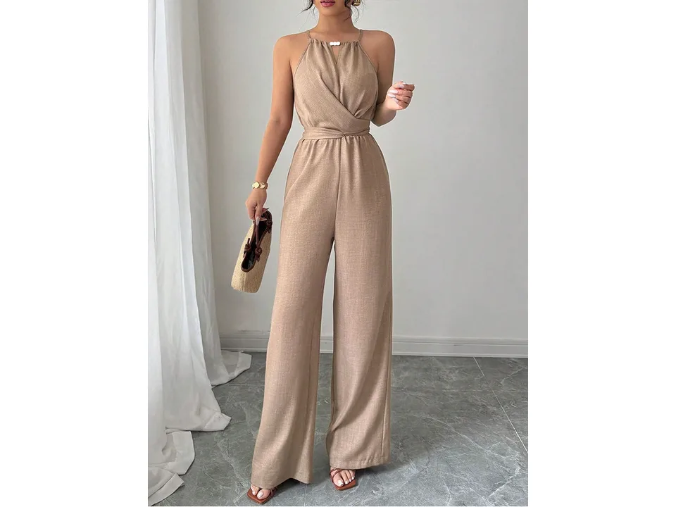 A model wearing a beige sleeveless jumpsuit and holding a small bag.