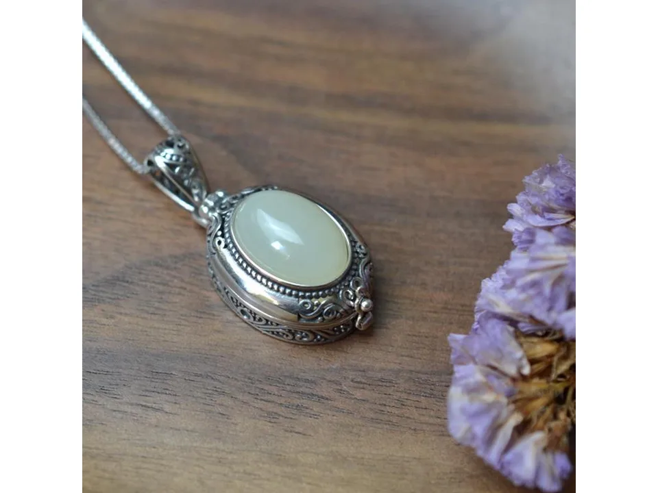 Close-up of the silver and jade locket pendant resting on a wooden surface next to dried flowers.