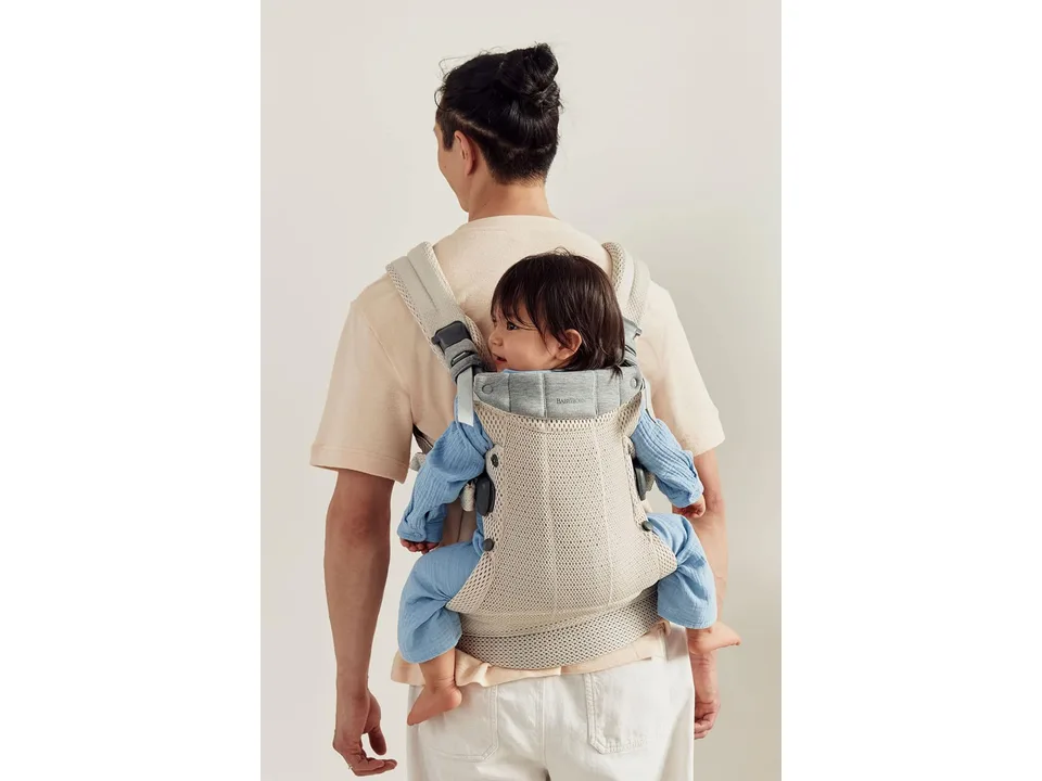 A man wearing a beige baby carrier with a baby facing inward on his back.