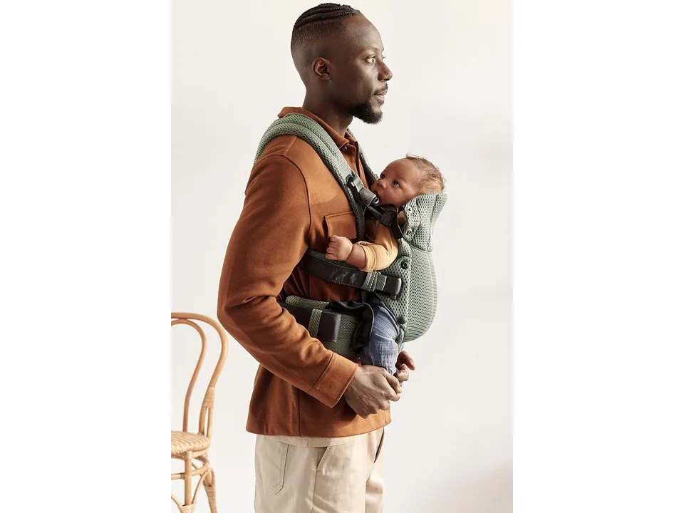 A man wearing a green baby carrier with a baby facing inward on his chest.