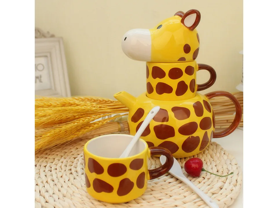 Giraffe ceramic tea set with a teapot, stacked mug, and an additional mug with a spoon on a woven mat.