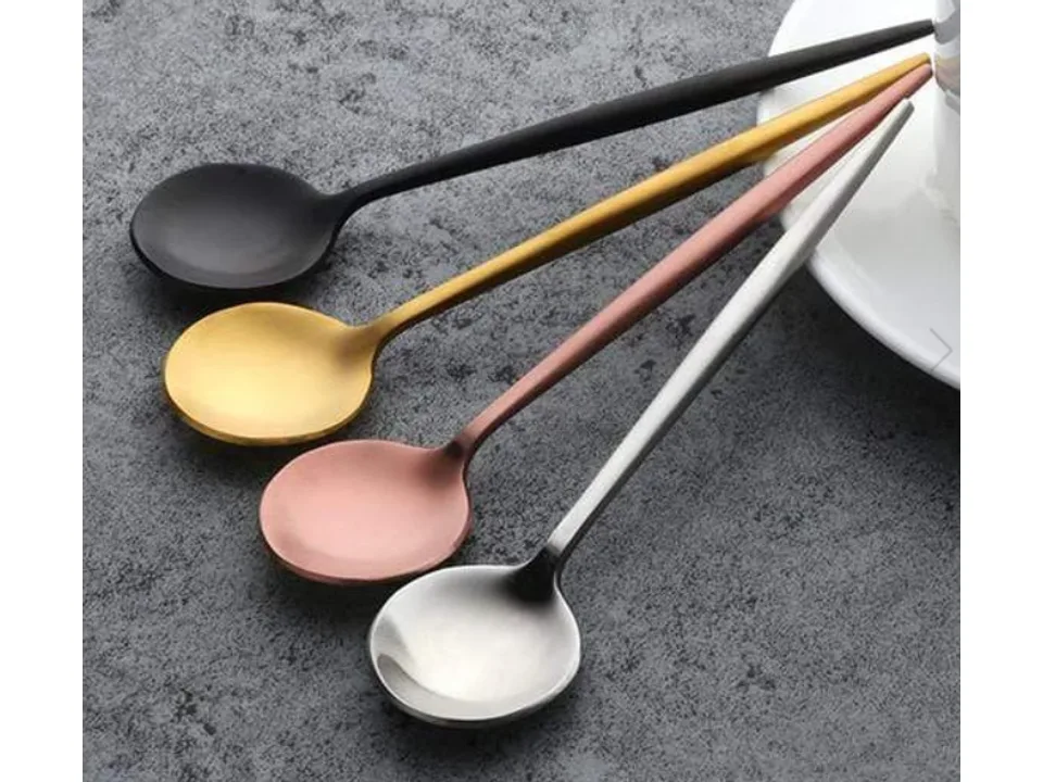 Four stainless steel spoons in different colors resting on a textured surface.