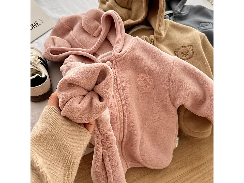 Close-up of a pink fleece hoodie showing the soft texture and a small embroidered rabbit face.