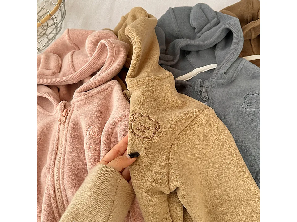 Close-up of a tan fleece hoodie showing the embroidered bear face detail.