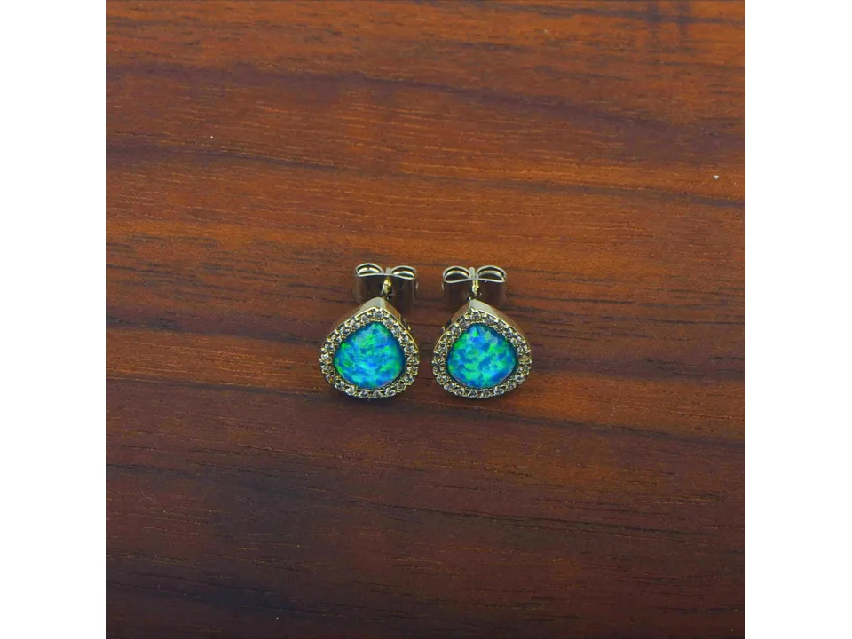 A pair of blue opal teardrop stud earrings on a dark wooden surface.