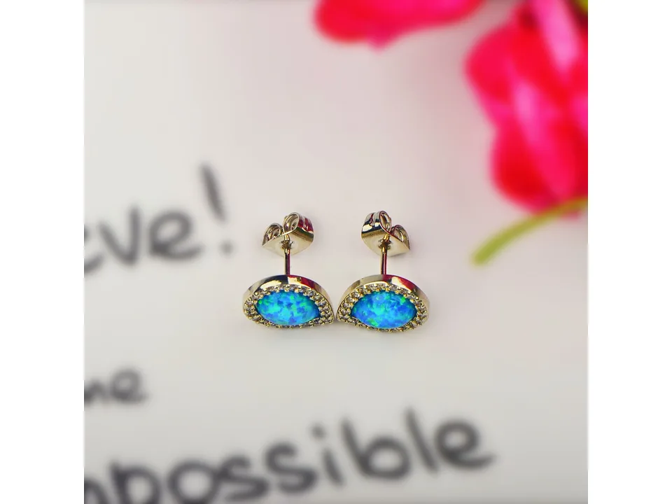 A pair of blue opal teardrop stud earrings on a white background with blurred text.
