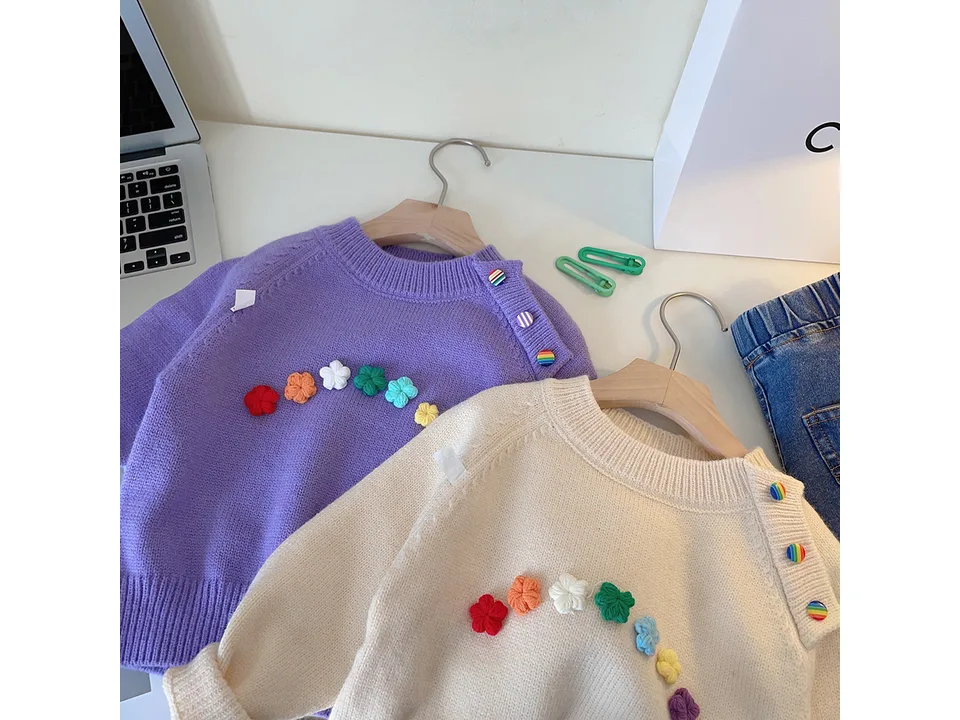 Purple and cream children's sweaters with colorful floral appliques and shoulder buttons.