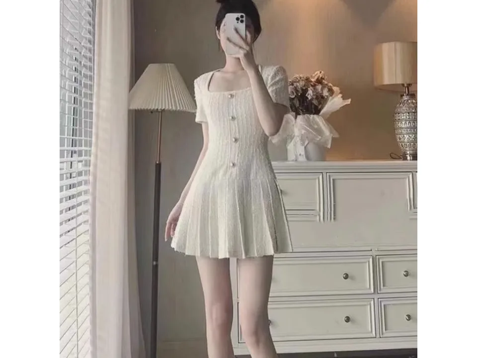 A woman wearing a white square neck mini dress with a pleated skirt.