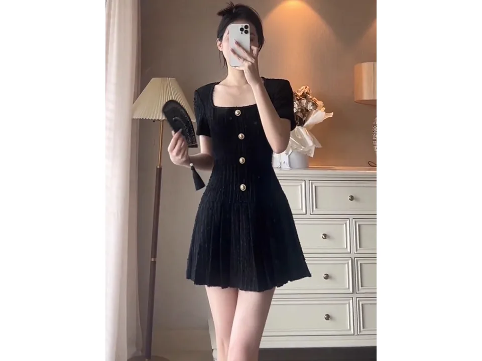 A woman wearing a black square neck mini dress with a pleated skirt.