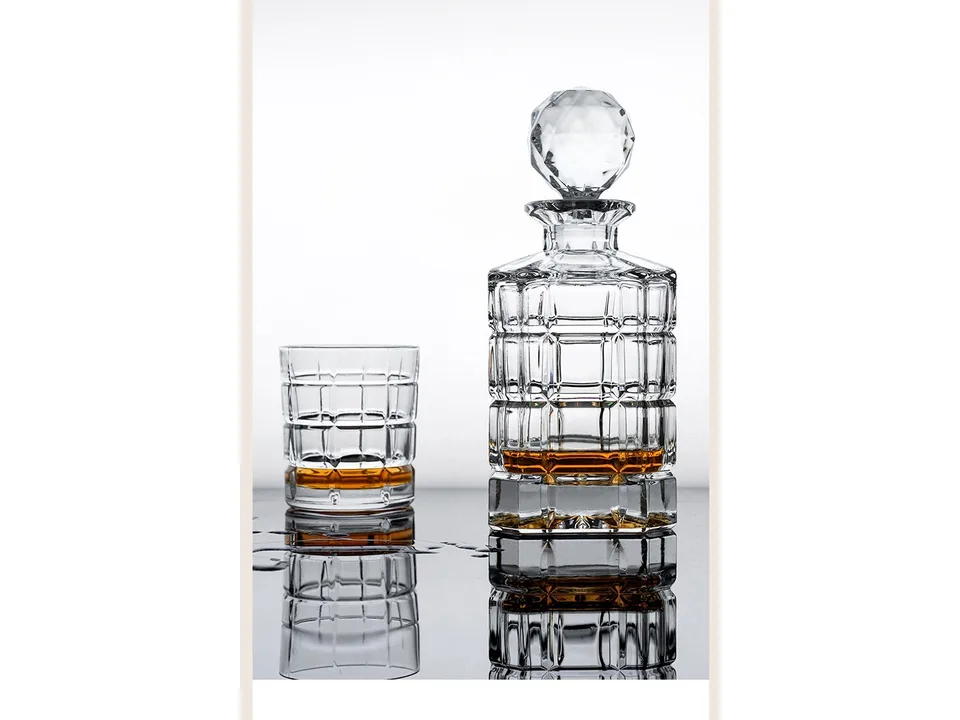 Crystal whiskey decanter and glass set on a reflective surface.