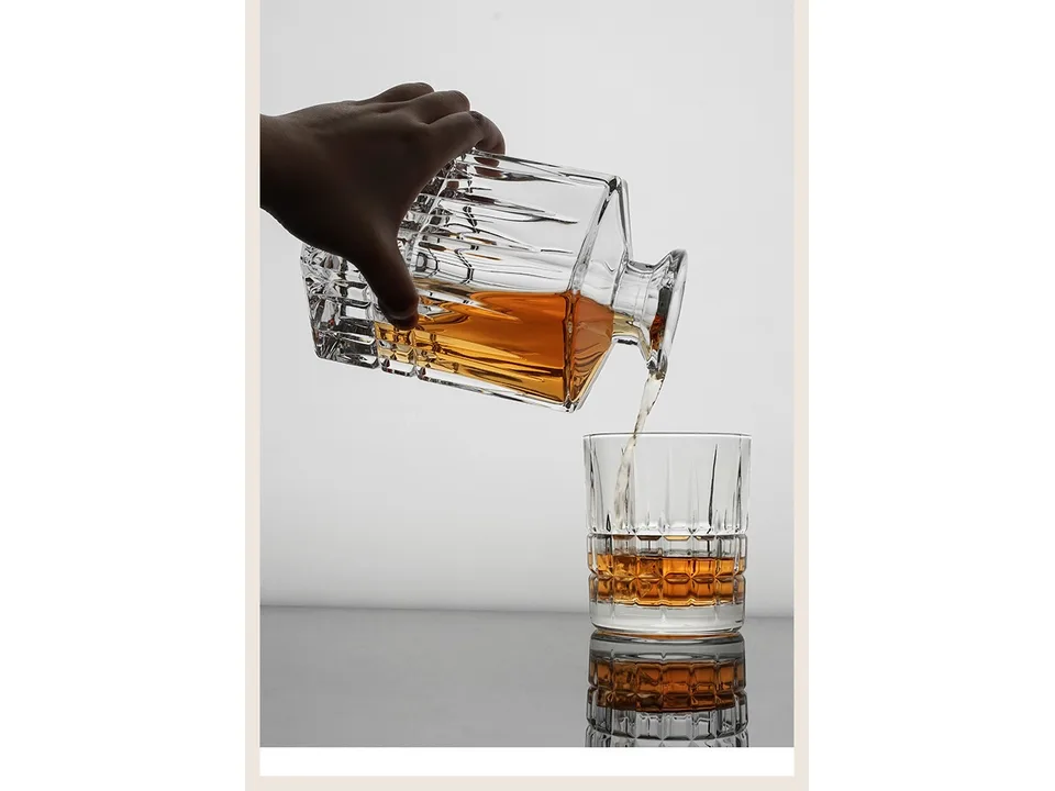 Hand pouring whiskey from the crystal decanter into a matching glass.