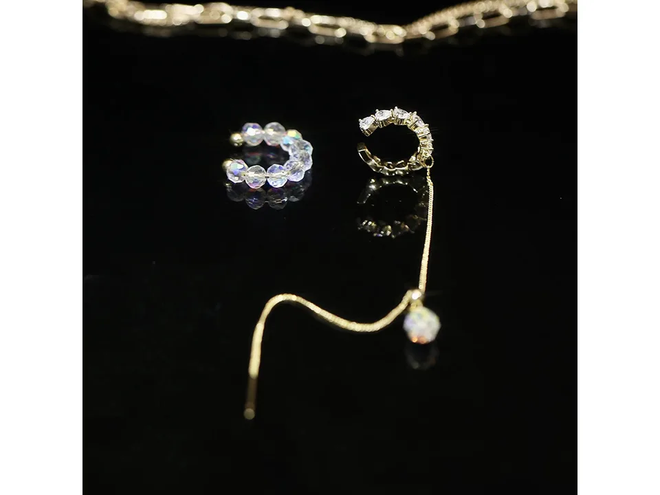 Two crystal ear cuffs, one with a chain and drop charm, on a black background.