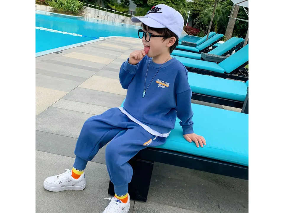 A young boy wearing a blue long-sleeve sweatshirt and matching jogger pants by a swimming pool.