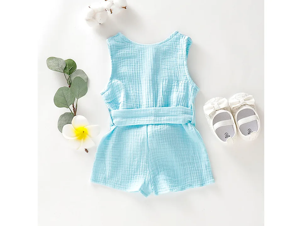 Light blue sleeveless toddler jumpsuit with a bow belt, displayed with decorative shoes and flowers.