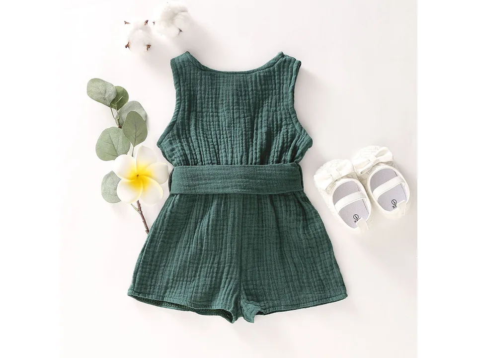 Dark green sleeveless toddler jumpsuit with a bow belt, displayed with decorative shoes and flowers.