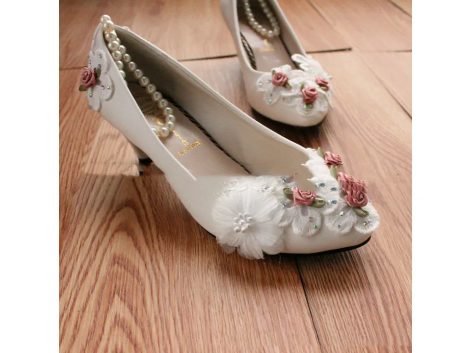 Side view of white wedding pumps with floral embellishments and pearl anklet.