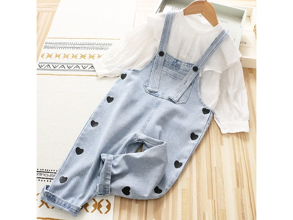 Denim overalls styled with a white long-sleeve blouse.