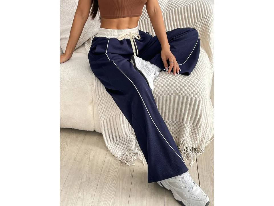 Model sitting down wearing navy blue wide-leg sports trousers.