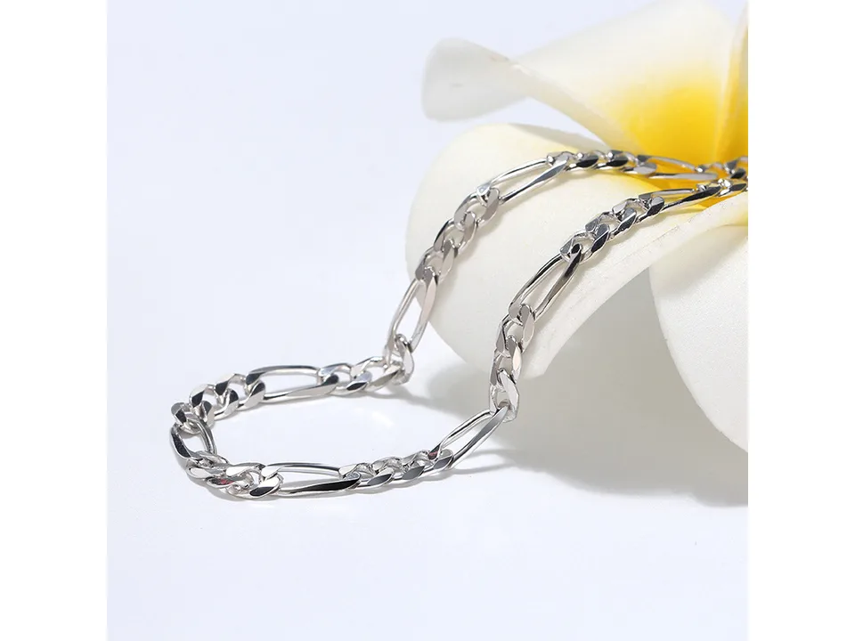 A silver Figaro chain necklace resting on a white flower petal.