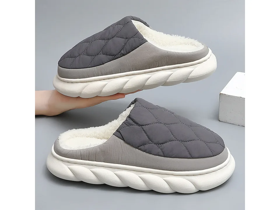 A pair of grey quilted slippers with white fleece lining being held up.