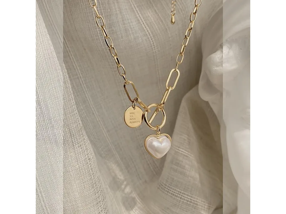 Close-up of a gold chain necklace with a heart-shaped pearl pendant and a toggle clasp.