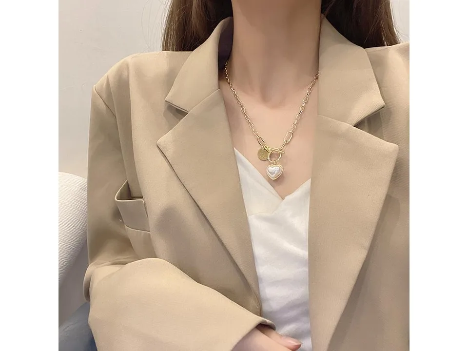 A woman wearing the gold heart pendant necklace with a beige blazer.