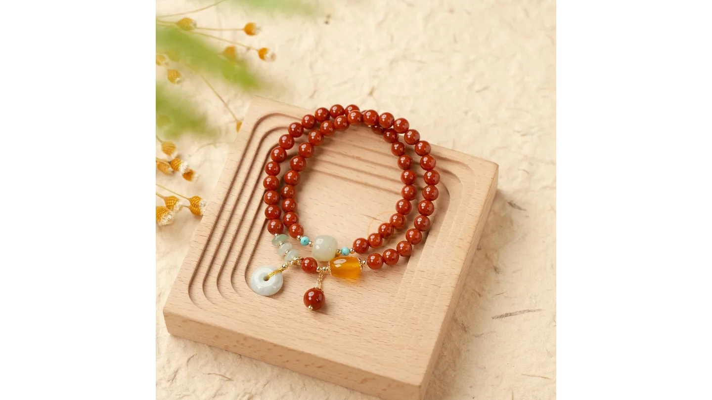 A red beaded bracelet with jade and yellow stone accents resting on a wooden display stand.