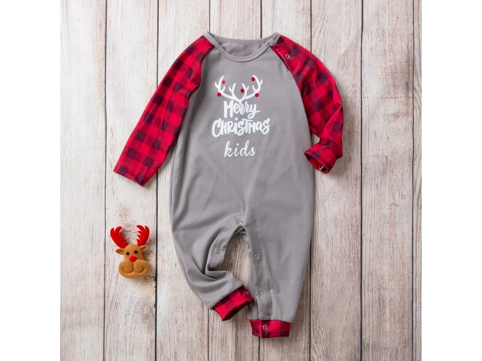 Baby Christmas romper with a small plush reindeer toy on a wooden background.