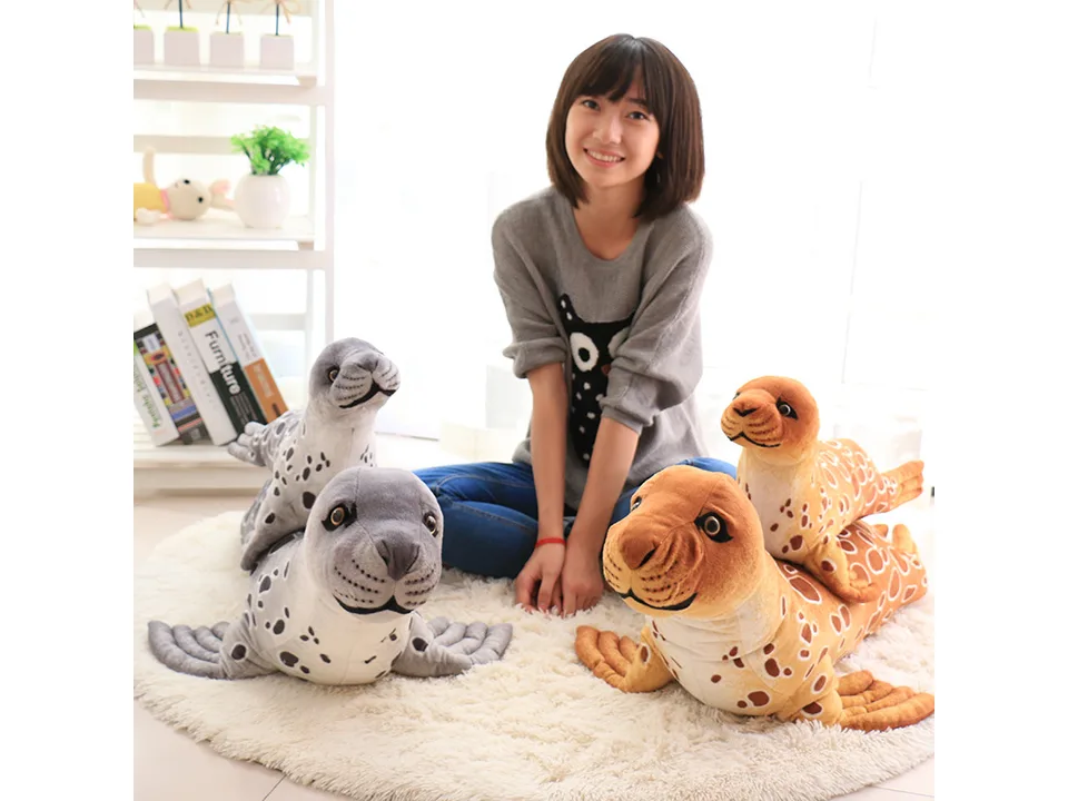 A person sitting on a rug with a grey and a brown plush seal toy.