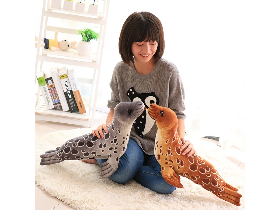 A person holding a grey and a brown plush seal toy.