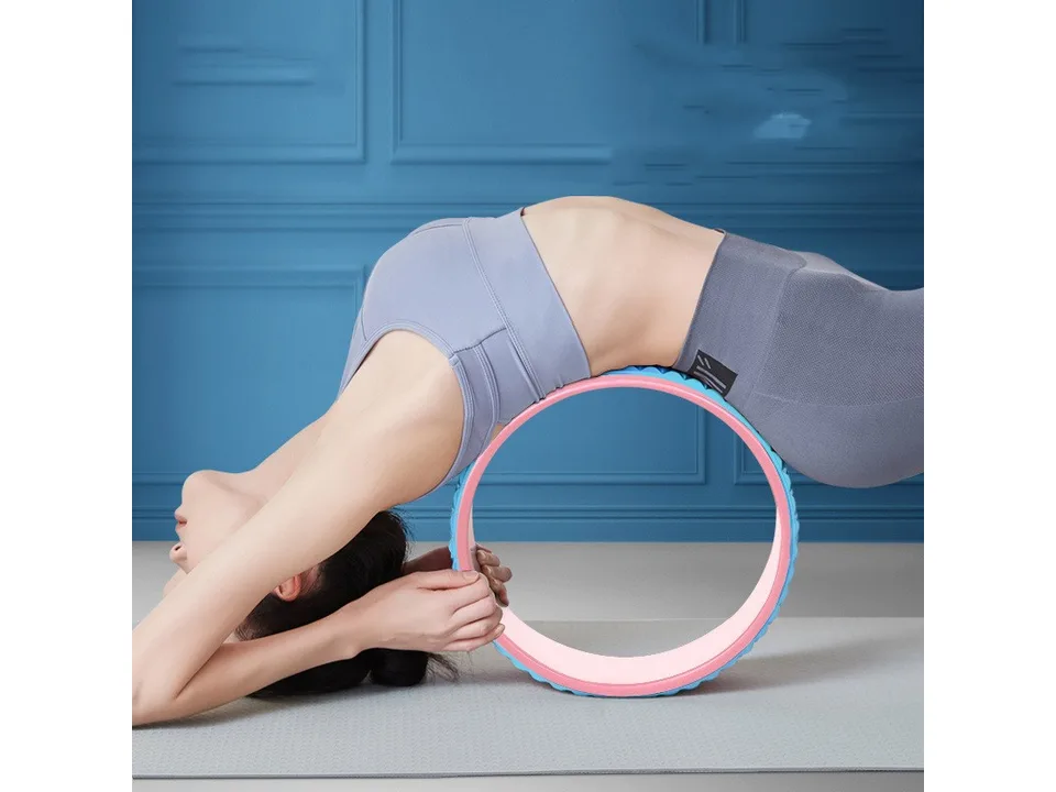 Woman performing a yoga pose with a blue and pink yoga wheel.