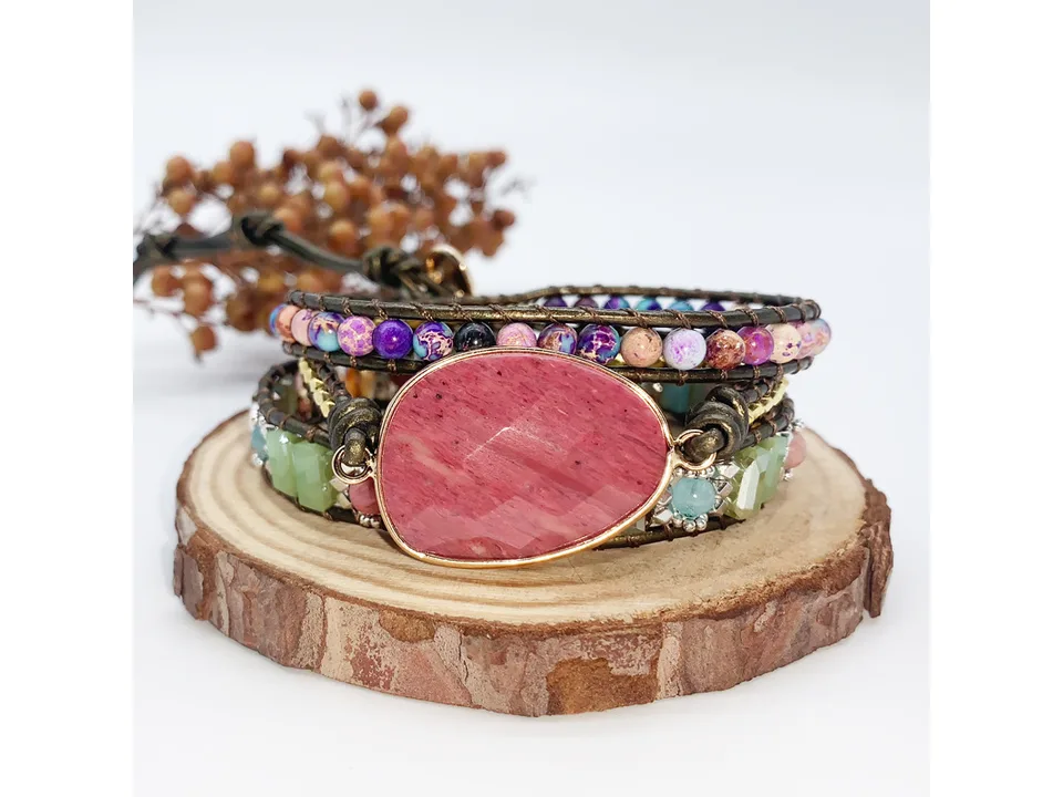 Multi-layer leather bracelet with natural stone beads and a large pink center stone on a wooden base.
