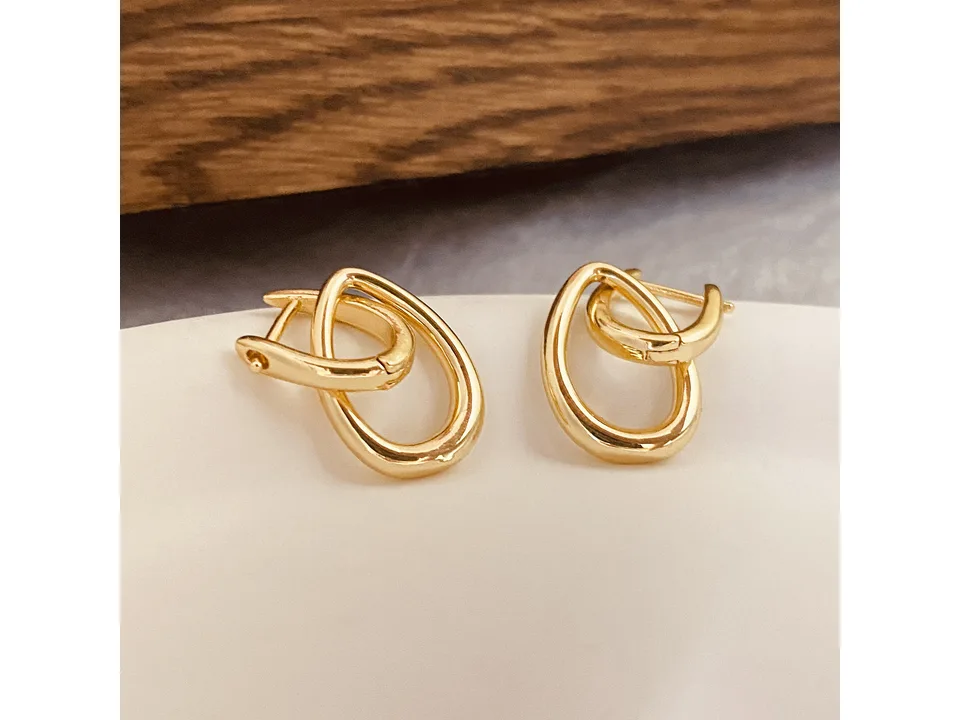 Pair of gold interlocking drop earrings on a white surface.