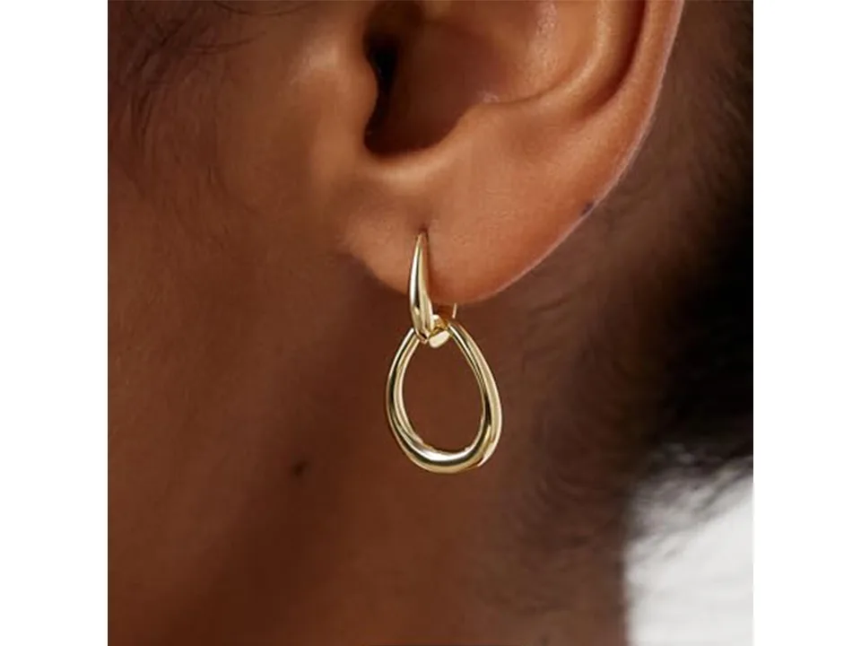 Gold interlocking drop earrings worn on an earlobe.