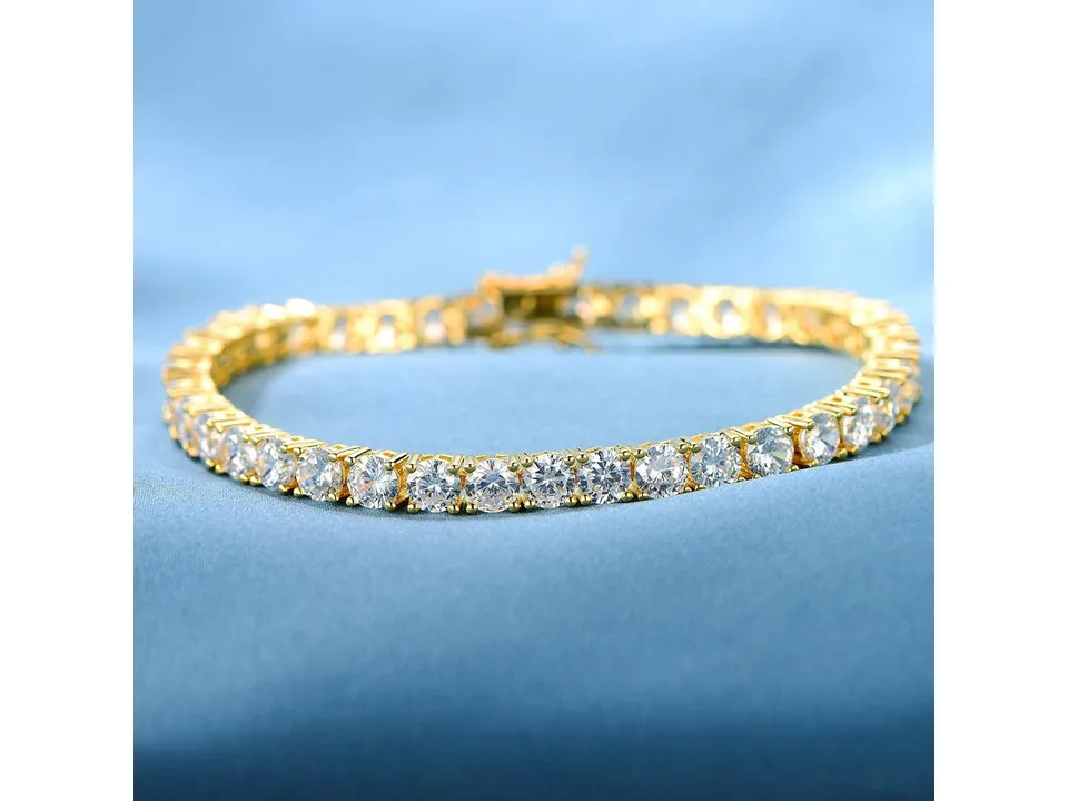 Gold tennis bracelet with cubic zirconia stones on a blue fabric background.