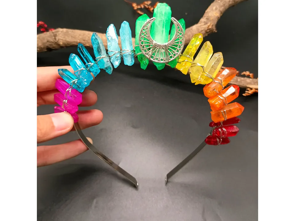 Hand holding a rainbow crystal crown headband with a crescent moon charm.
