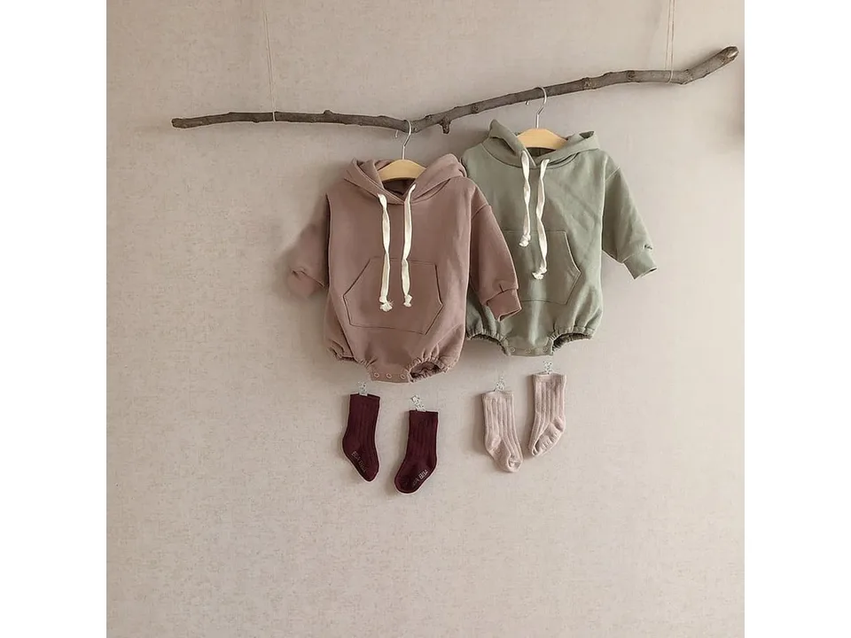 Two baby rompers in sage green and brown hanging on a wooden branch with matching socks.