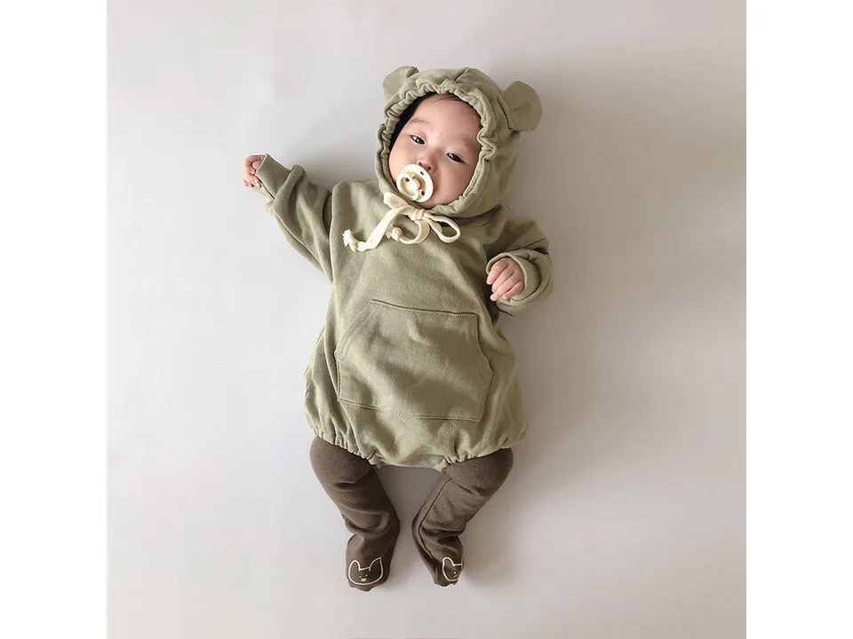 Baby wearing a sage green bear-eared hooded romper with footed leggings.