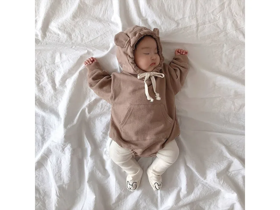 Baby sleeping while wearing a brown bear-eared hooded romper with white leggings.