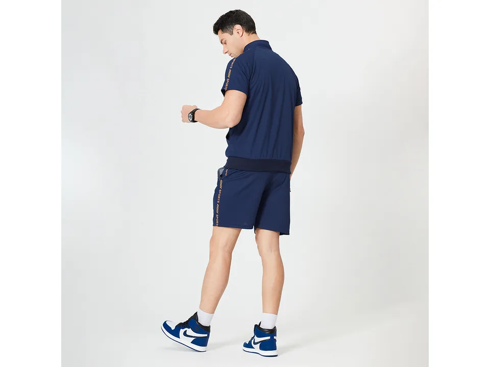 A man wearing a blue athletic short sleeve zip-up top and matching shorts, viewed from the back.
