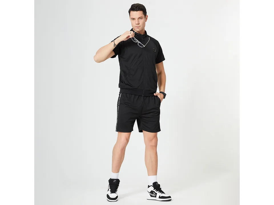 A man wearing a black athletic short sleeve zip-up top and matching shorts, viewed from the front.