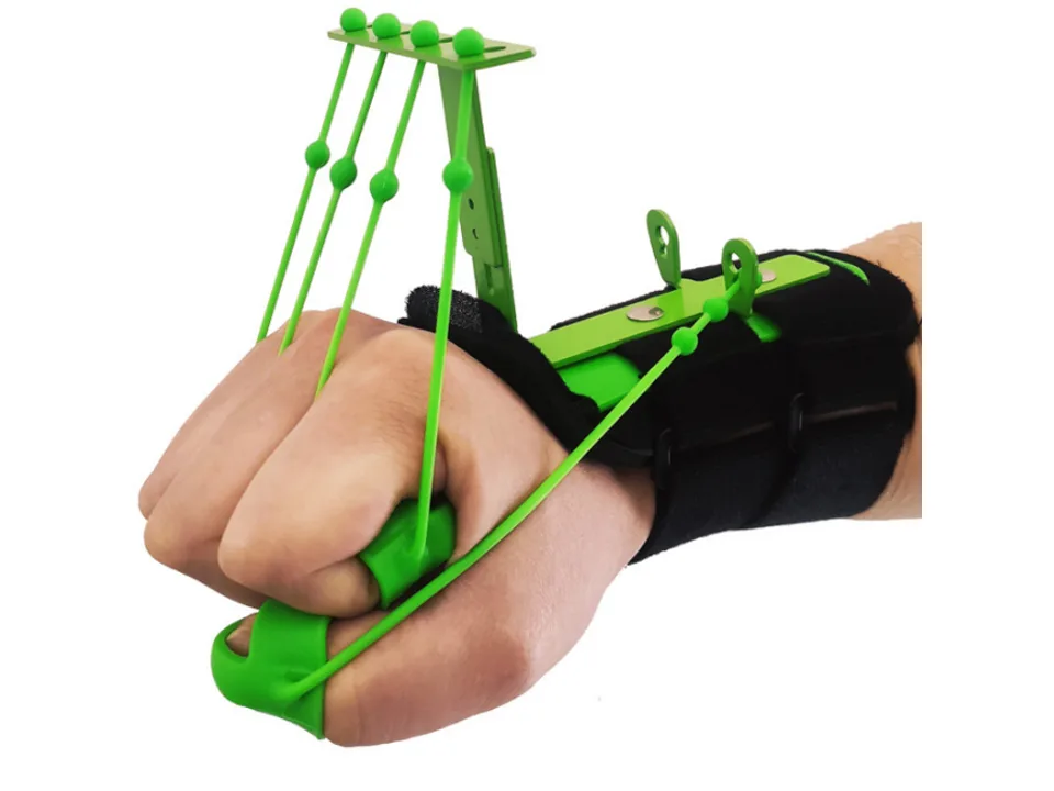 A hand wearing a green finger and wrist extensor trainer, with fingers curled into a fist.